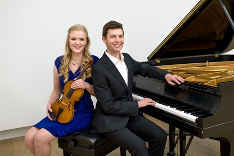 an image of a male pianist sitting on his bench to the left of the piano and to his left, also seated on the bench, is a woman with a violin