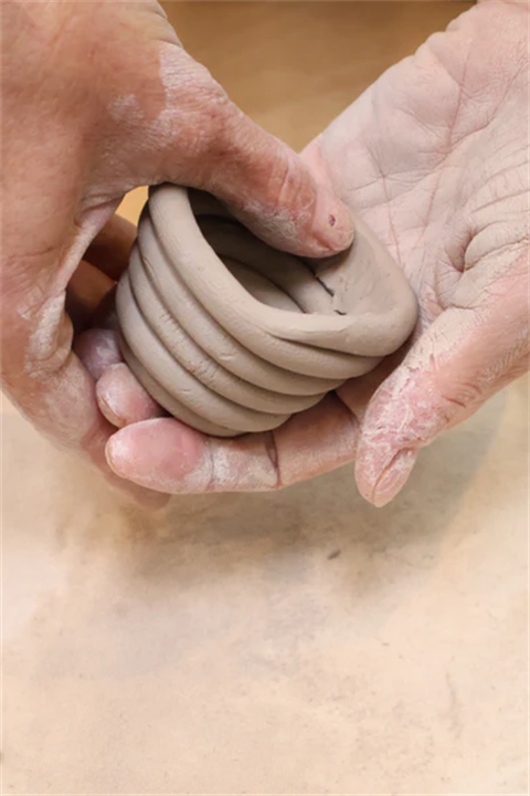 Two hands craft clay into a pot with a coiling patern.