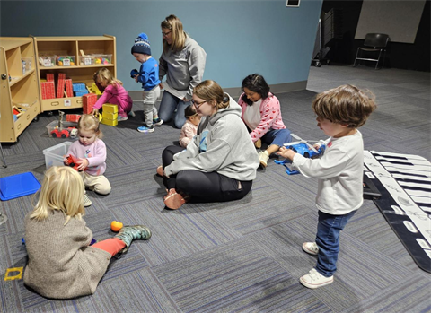 an image of preschool-age children and three caregivers playing with toys