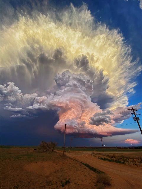 A large cloud at sunset looms over a street.